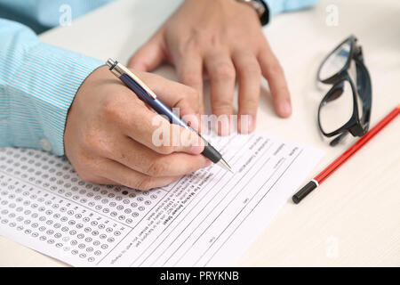 Man is filling OMR sheet heading with pen. Picture of glasses and pencil on the table Stock Photo