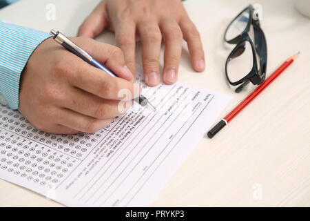 Picture of man is filling OMR sheet heading with pen. Picture of glasses and pencil on the table. Stock Photo