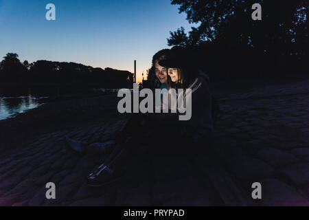 Young couple using tablet at the riverside in the evening Stock Photo