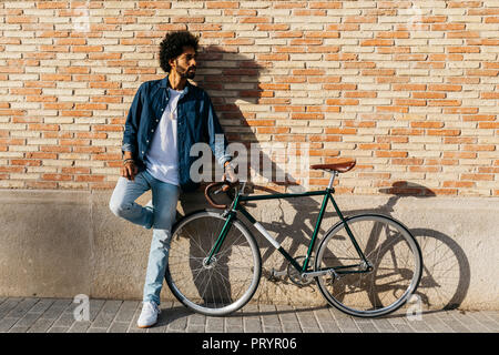 Young man with racing cycle leaning against brick wall Stock Photo