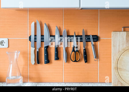 Knives hang on a magnet holder. Orange kitchen wall. A method of storing sharp objects in the kitchen Stock Photo
