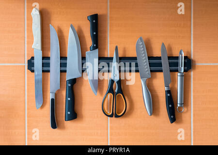 Knives hang on a magnet holder. Orange kitchen wall. A method of storing sharp objects in the kitchen Stock Photo