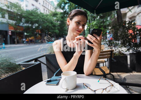 Young woman sitting in cofee shop, using smartphone Stock Photo