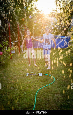 Brother and sister having fun with lawn sprinkler in the garden Stock Photo