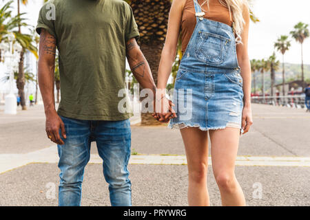 Spain, Barcelona, multicultural young couple holding hands on promenade, partial view Stock Photo