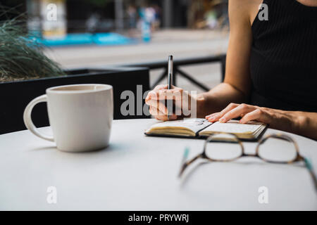 Young woman sitting in coffee shop, brainstorming, writing notes in notebook Stock Photo