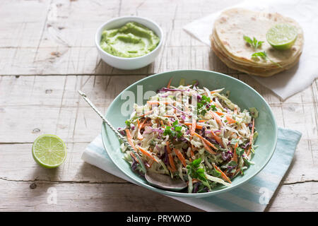 Coleslaw made from cabbage, carrots and various herbs, served with tortillas and guacamala on a wooden background. Stock Photo