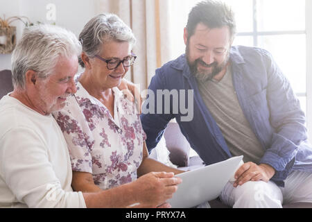 family team at work at home sit down on the sofa. smile and have fun working on a laptop together. mother father and son aged senior use technology an Stock Photo