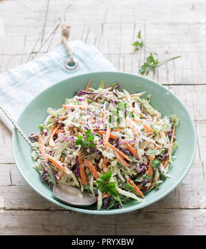 Coleslaw of cabbage, carrots and various herbs with mayonnaise in a large plate on a wooden background. Stock Photo