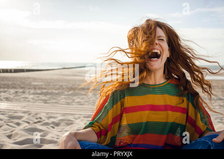 Woman sitting on the beach, screaming for joy Stock Photo