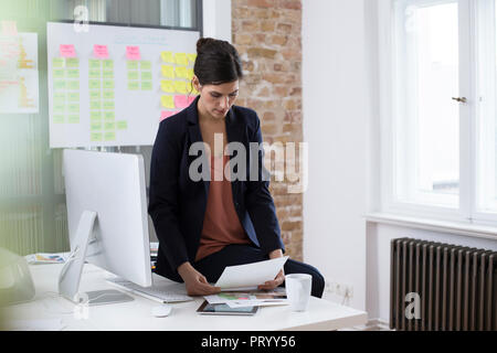 Businesswoman at desk in office looking at printouts Stock Photo