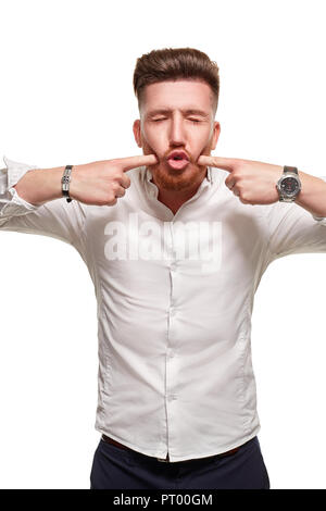 Handsome man wearing a white shirt, pressing on cheeks by his fingers, standing on a white background. Stock Photo