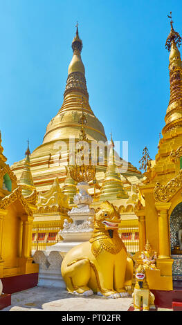 The large statue of chinthe (leogryph) among the outer stupas of Shwedagon with its main pagoda on background, Yangon, Myanmar. Stock Photo