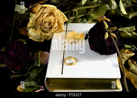 White Holy Bible, one wedding ring and dry roses. Touching conceptual image of marriage, death and 'till death do us part' wedding vow.