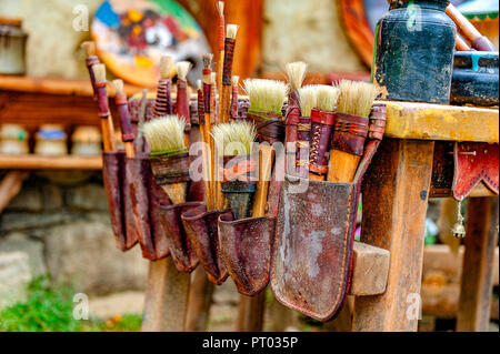 ARTIST's POUCH OF PAINT BRUSHES. Rustic painter’s brushes of various shapes and sizes in an old leather pouch attached to one side of a table. Stock Photo