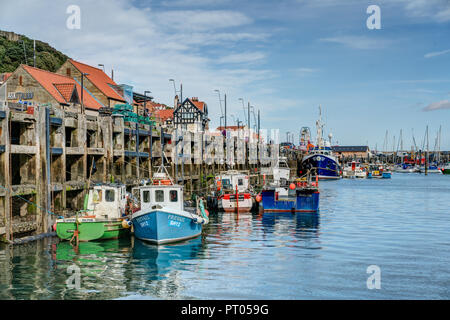 A tranquil picture of colourful fishing boats moored in Scarborough harbour against the wooden quayside structure on a calm beautiful summers day. Stock Photo
