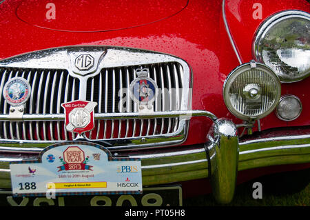 Front bonnet and radiator grill of bright red MG sports car showing headlights and various MG drivers badges showing raindrops Stock Photo