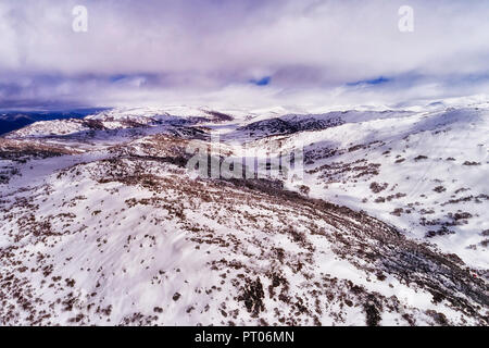 WHite snow slopes of the highest mountains in Australia under white clouds along Perisher valley with thick snow and ski resort sports tracks. Stock Photo