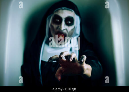 closeup of a frightening evil nun, wearing a typical black and white habit, with a threatening gesture, emerging from a white coffin Stock Photo