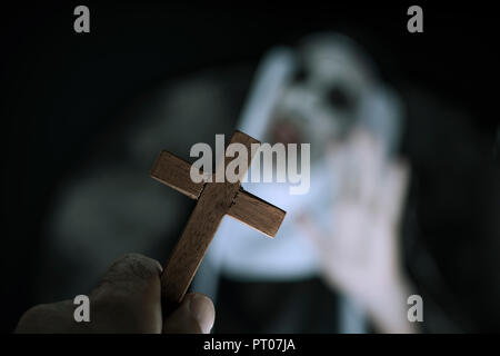 closeup a cross in the hand of a man and a frightening evil nun, wearing a typical black and white habit, screaming Stock Photo
