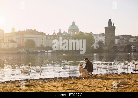 Morning walk with dog. Young man and his labrador retriever on riverbank against Old Town with Charles Bridge in Prague. Stock Photo