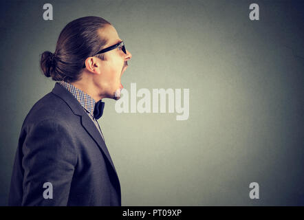 Side view of an angry man in rage shouting loudly with mouth opened on gray background. Stock Photo