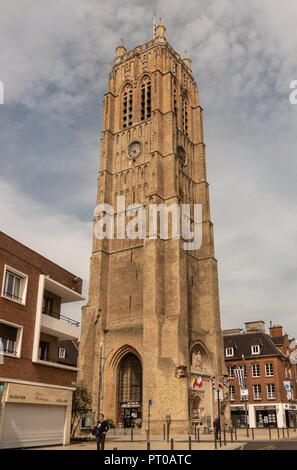 Dunkerque, France - September 16, 2018: the brown brick Belfry of Dunkirk towers over houses under cloudy blue sky. Street scene with people. Stock Photo