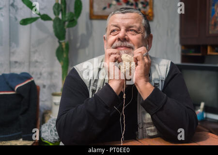 Indoor portrait of positive Ukrainian peasant listening music over headphones and taking clew of thread while sitting at old table Stock Photo