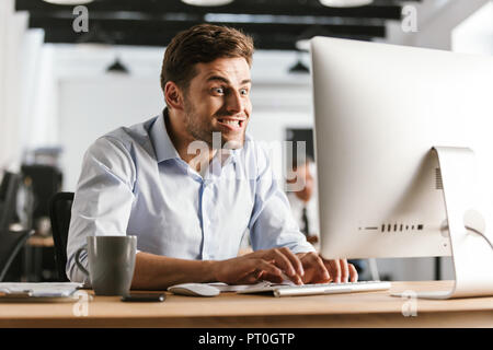 Image of Funny business man using computer while sitting by the table in office Stock Photo