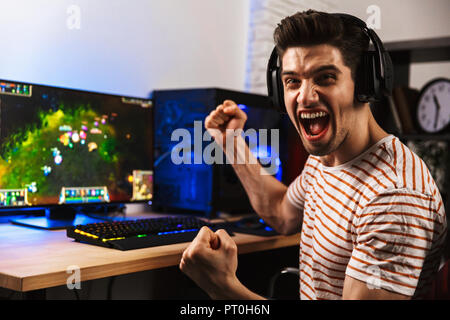 Portrait of happy man playing video games on computer wearing headphones and using backlit colorful keyboard Stock Photo