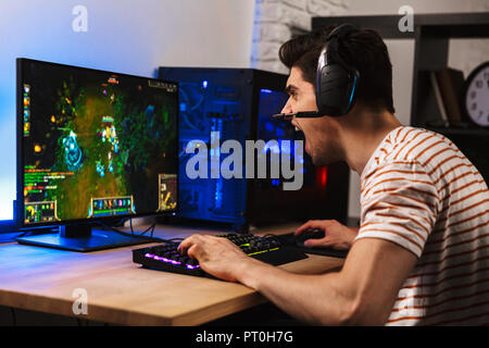 Portrait of angry gamer guy wearing headset yelling while playing video games on computer Stock Photo