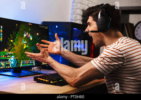 Portrait of stressed disappointed man wearing headset screaming while playing video games on computer Stock Photo