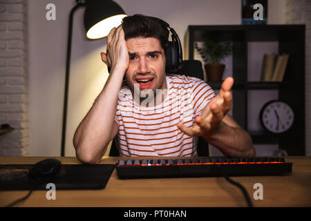 Confused gamer playing video games on computer while sitting by the table at home Stock Photo