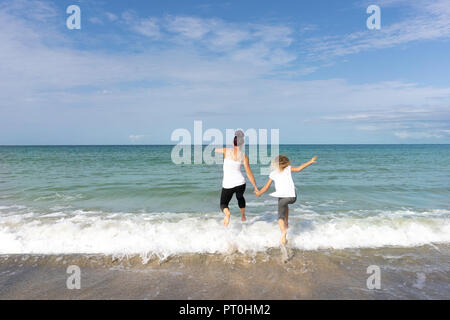 Mother and Daughter jumping over waves into sea at the gorgeous St Ives in Cornwall, UK, the stunning Carbis Bay Stock Photo