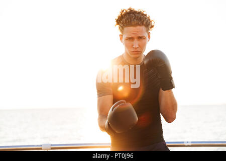 Focused young sportsman in boxing gloves training outdoors Stock Photo