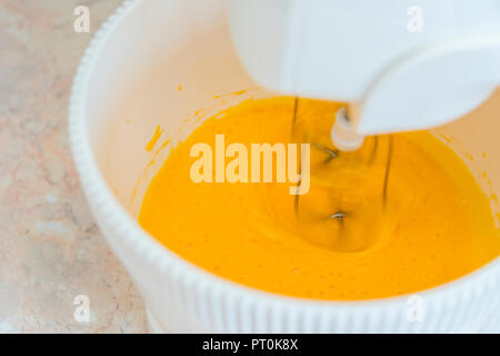 Electric Mixer Beaters Beating Eggs. Cooking, whipping eggs with electric whisk in bowl, close up. Stock Photo