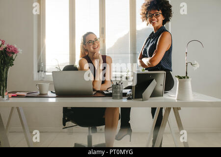 Portrait of two young businesswoman at desk in modern office. business partners looking at camera and smiling in office. Stock Photo