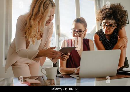 Three beautiful creative business woman working with laptop and watching something on tablet in office. Group of businesswoman working over a new proj Stock Photo