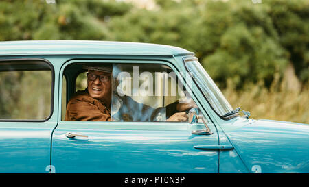 Senior man driving a classic car. Old man looks out of the window of his car before making a turn on road. Stock Photo