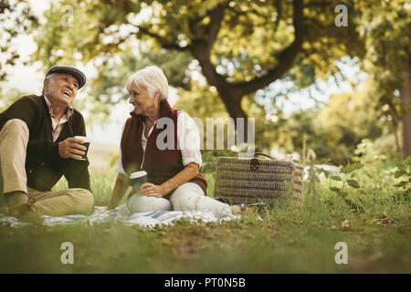 Portrait of beautiful senior couple sitting on blanket outdoor enjoying time together. Old couple picnicking on weekend holiday. Stock Photo