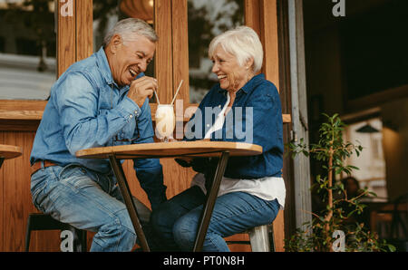 Cheerful old couple sitting at cafe having a coffee. Senior man and woman sitting at restaurant table talking with cold coffee on table. Stock Photo