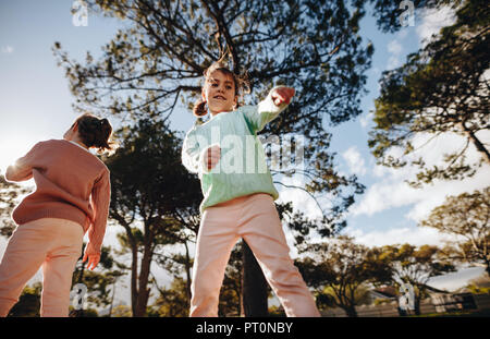 Low angle view of little girl dancing at the park with her sister standing by. Small girls having fun at the playground outdoors. Stock Photo