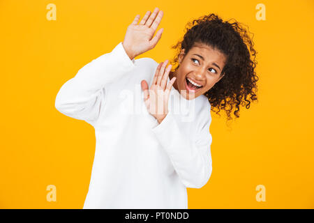 Portrait of a scared young african woman standing isolated over yellow background, protecting herself with hands Stock Photo