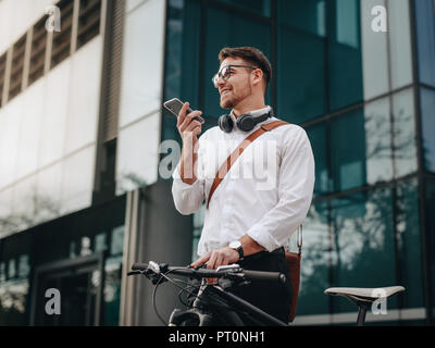 Man holding his bicycle and talking over mobile phone while walking to office. Smiling businessman speaking on cell phone while going to office in the Stock Photo