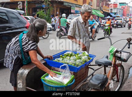 Elderly woman with curved spine selling limes from her rickshaw. Bangkok, Thailand. Stock Photo