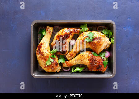 Baked chicken legs in baking tray on blue stone background with copy space. Top view.