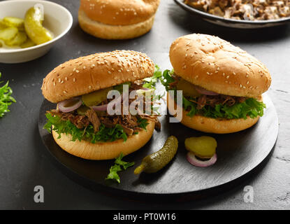 Tasty pulled beef sandwiches with marinated cucumber, onion, greens on black wooden board Stock Photo