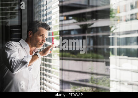 Businessman peeking through sunblinds at the window in office Stock Photo