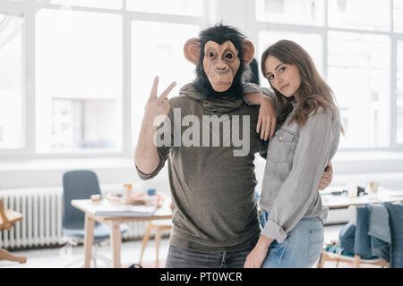 Man wearing chimpanzee mask, making victory-sign, woman leaning on him Stock Photo