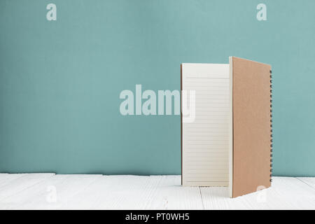 Blank notebook on white wood table front green wall background with copy space for add text or advertising word, menu mockup. Stock Photo